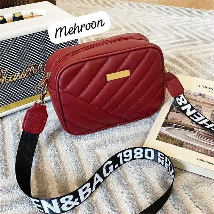 Red quilted handbag with a black strap on a textured surface