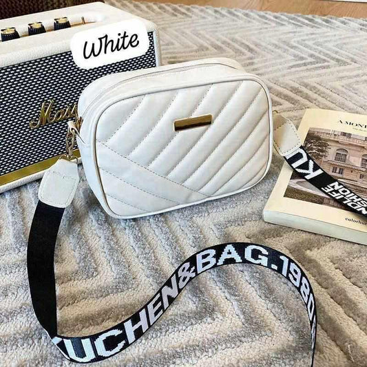 White quilted handbag with a black strap on a textured surface